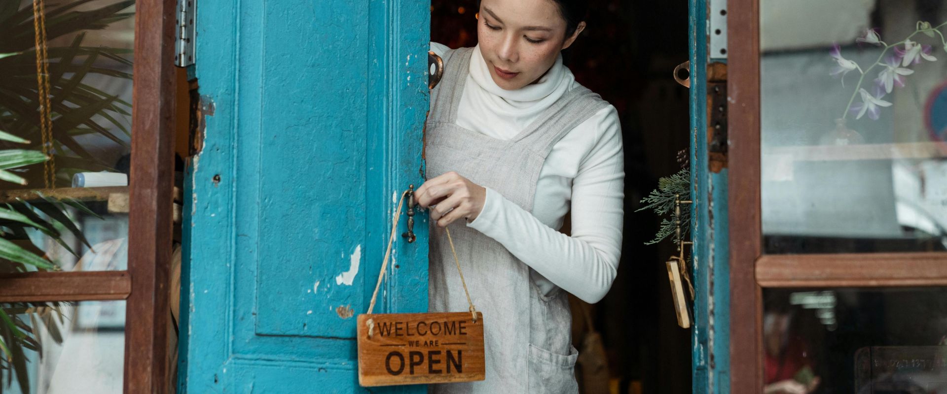 A woman adjusts an open sign on a blue wooden door of a cafe inviting customers inside.