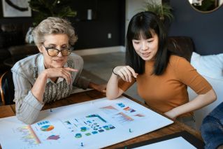 Two women discussing charts at a modern office desk, showcasing business collaboration.