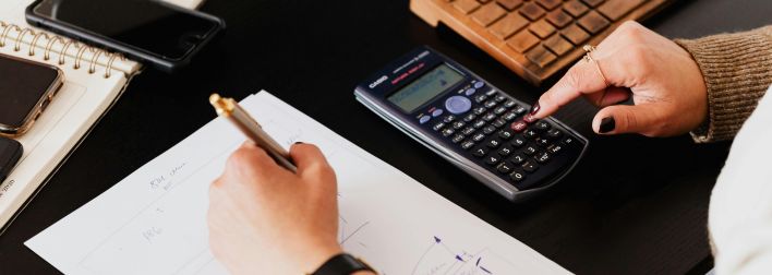 Close-up of hands working with a calculator and notebook on a desk, analyzing documents.